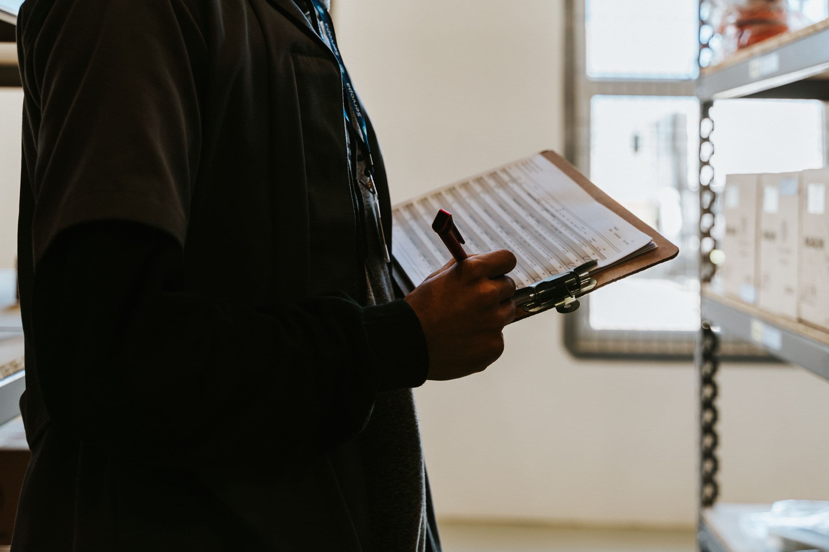 Сотрудник с планшетом и ручкой сверяет список у стеллажей с коробками